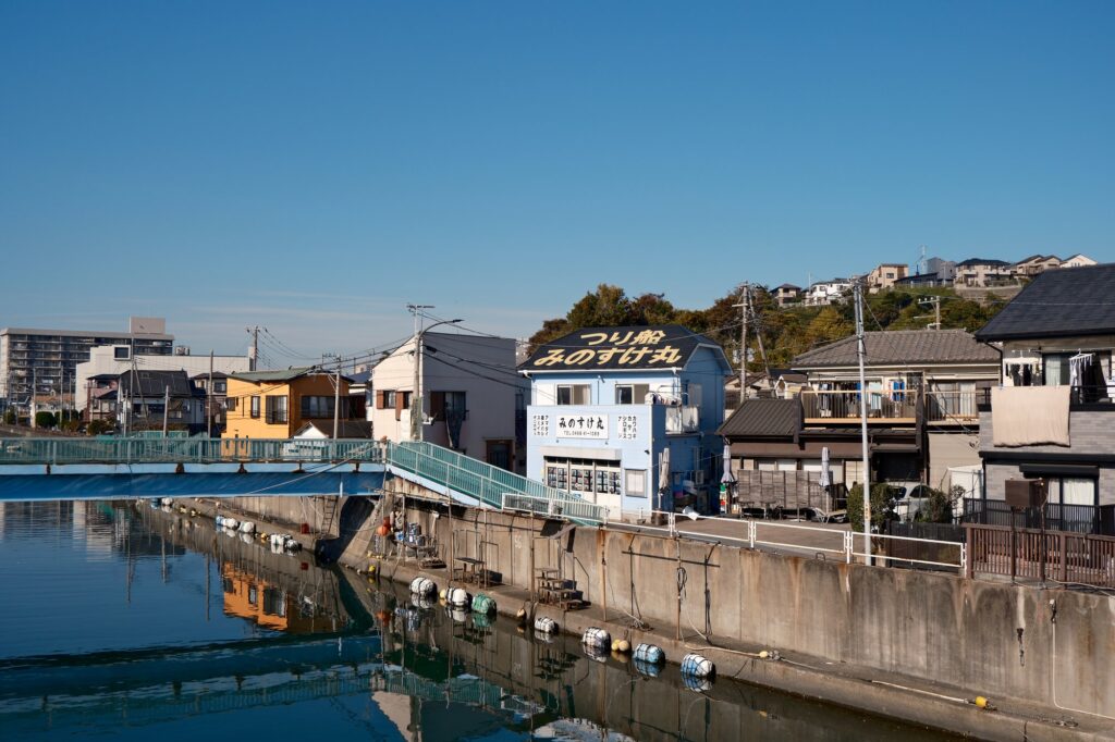 青空の下、釣り船屋の看板と水面に映る家並み